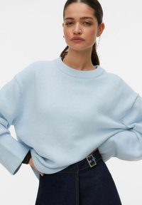 Pull en maille bleu clair avec un col rond et des manches larges, associé à une jupe en denim foncé avec une boucle de ceinture visible.