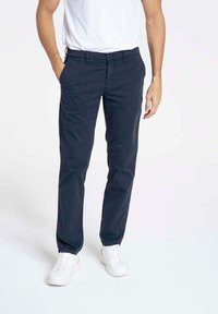 Chinos en coton navy avec une coupe droite, dotés de poches et de détails de couture subtils, portés avec des baskets blanches et un t-shirt basique blanc.