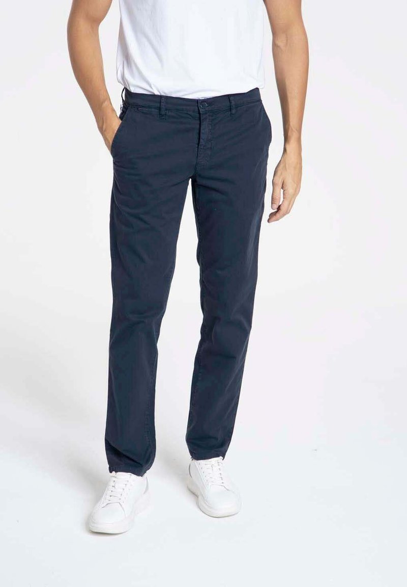 Chinos en coton navy avec une coupe droite, dotés de poches et de détails de couture subtils, portés avec des baskets blanches et un t-shirt basique blanc.