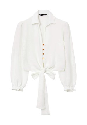 Blusa bianca con maniche lunghe e a sbuffo, colletto e un fiocco in vita. Presenta dettagli con bottoni lungo la parte anteriore realizzati in materiale marrone.