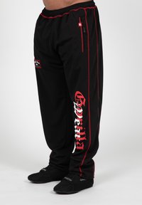 Zwarte sportbroek met rode strepen, voorzien van een grafisch logo aan de zijkant, elastische tailleband en een ritszak. Getextureerde stof.