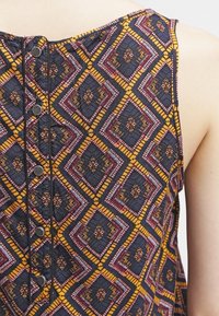 Tissu à motifs multicolores présentant un design géométrique en jaune, rouge et bleu. Comprend une patte de boutonnage à l'arrière.