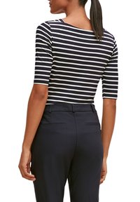 Chemise rayée bleu marine et blanche avec un décolleté bateau et des manches trois-quarts, assortie à un pantalon sombre avec des poches arrière.