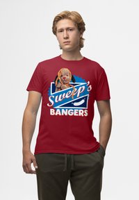 Rød bomulds T-shirt med et grafisk design med blå accenter og teksten "Sweep's Bangers." En plysdog er placeret på T-shirten.