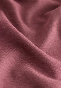 Weiche Nahaufnahme von zerknittertem malvenfarbenem Stoff, der eine feine Strickstruktur und subtile Falten zeigt.