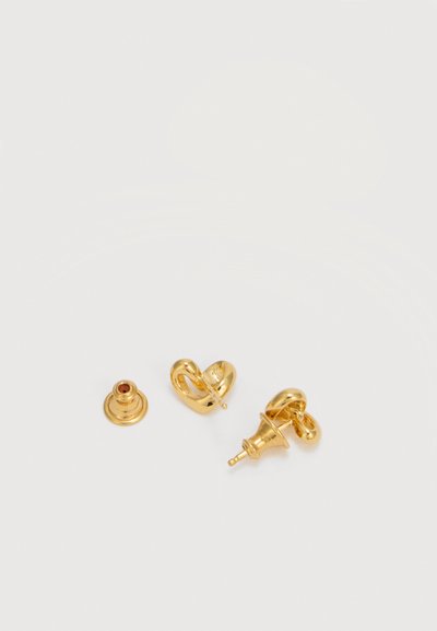 Pequeños pendientes de oro en forma de corazón con cierre tipo mariposa sobre un fondo blanco.