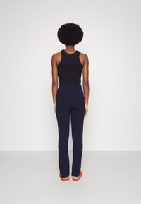 Svart ärmlös topp i kombination med marinblå byxor med rand. Byxorna har en åtsittande midja och en rak bendesign.