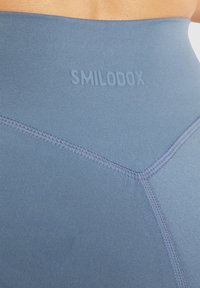 Hooggeribbelde blauwe leggings van glad, rekbaar materiaal, met een subtiele merkreferentie en versterkte stiksels langs de naden.