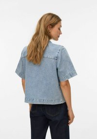 Lyseblå denimjakke med korte ermer, ryggstykke og rå kant. Stoffet har en myk tekstur og synlige sømmer.