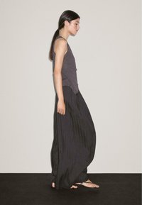 Dark gray sleeveless top, paired with black vertical striped wide-leg pants. The fabric appears soft and flowy, with simple sandals.