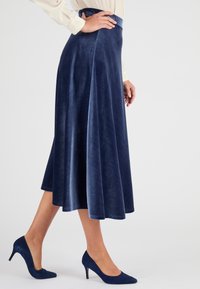 Falda midi de terciopelo azul marino con una forma acampanada y textura suave, combinada con zapatos de tacón a juego.