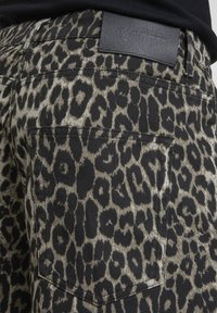 Gros plan sur un pantalon à imprimé léopard avec une étiquette en cuir noir portant l'inscription "2Y STUDIOS" au-dessus de la poche arrière.