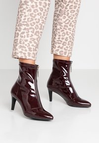 Bottines bordeaux en cuir verni avec bout pointu et fermeture éclair latérale. Les talons sont fins, d'environ 7,5 cm de hauteur, avec une finition lisse.