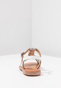 Bílé kožené sandály s hnědými podrážkami, nastavitelným páskem kolem kotníku a stříbrnými detaily. Plochý design s otevřenou špičkou a patou.