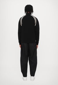 Svart hettegenser med hvite striper på skuldrene, kombinert med løstsittende svarte bukser og hvite joggesko.