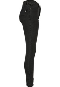 Vaqueros skinny negros de mezclilla, con tiro alto, diseño de cinco bolsillos y costuras mínimas. Textura suave con un ajuste ceñido.