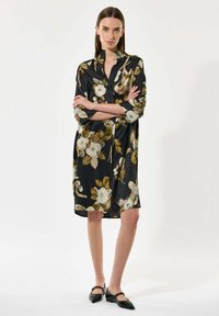 Czarna sukienka koszulowa z białym i żółtym nadrukiem kwiatowym, z długimi rękawami i kołnierzykiem. Gładki materiał o luźnym kroju, długość do kolan.