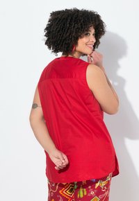 Blusa senza maniche rossa con taglio dritto e spalla posteriore. Tessuto in cotone morbido, senza motivi. Il modello indossa pantaloni colorati con motivi.