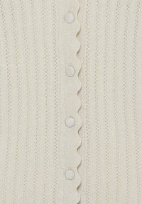 Tissu en maille crème avec des rayures verticales en œillets et un bord festonné présentant des boutons recouverts de tissu au centre.