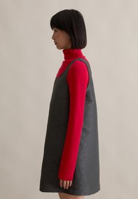 Γκρίζα υφασμάτινη φόρμα με χαλαρή εφαρμογή, σε στρώσεις πάνω από έναν φωτεινό κόκκινο ριγωτό ζιβάγκο. Η φόρμα διαθέτει φαρδιές τιράντες και απλό σχέδιο.