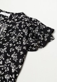 Schwarze Bluse mit floralem Muster aus weichem Stoff und Rüschensleeves. Sie hat kleine weiße Blumen und einen runden Ausschnitt.