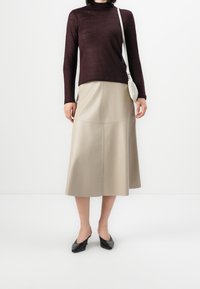 Haut bordeaux à manches longues avec un col montant, associé à une jupe en cuir beige de style trapèze. Chaussures à talons noires à bout pointu et sac texturé.