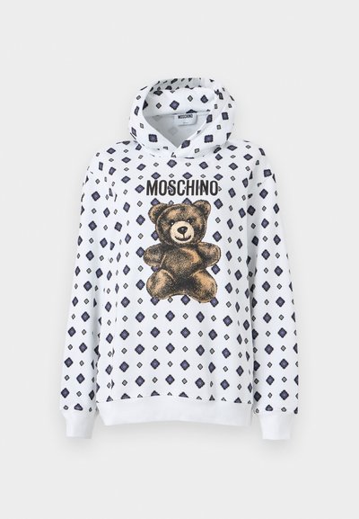 Sweat à capuche blanc avec un motif d'ours en peluche et des motifs en diamant bleu marine. Le matériau semble doux, avec des manches longues et une capuche à cordon de serrage.