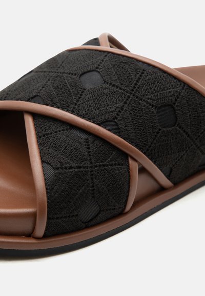 Μαύρο σανδάλι τύπου slip-on με υφασμάτινες λουρίδες με υφή εξαγώνου και καφέ επένδυση, μαλακή εσωτερική σόλα και επίπεδη εξωτερική σόλα.