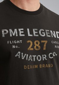 Sort bomulds t-shirt med grafisk print i hvid og guld, teksten inkluderer "PME Legend," "Flight No. 287," og "Aviator Co."