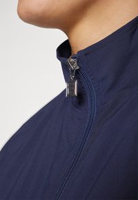 Navy blue zip-up jacket with a high collar, featuring a silver zipper pull and a smooth, textured fabric.