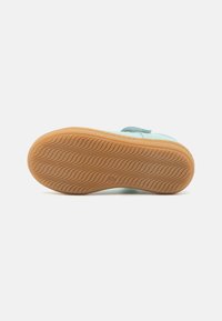 Semelle de chaussure présentant une surface en caoutchouc à motif ondulé de couleur beige clair, avec une partie supérieure bleue partiellement visible, mettant en avant le design de traction.
