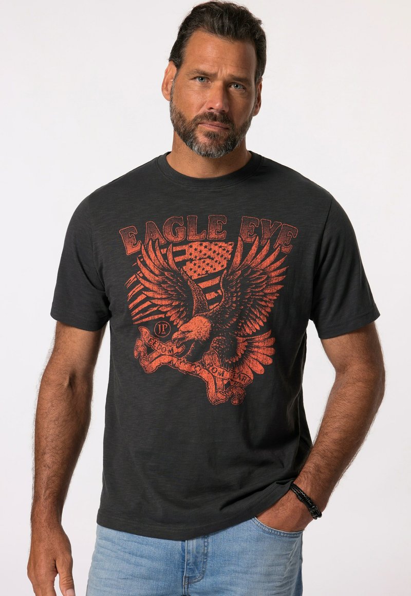 Zwarte ronde hals t-shirt met een rode adelaar grafiek en de tekst "EAGLE EYE," met een vervaagd ontwerp en zachte textuur. Korte mouwen, ontspannen pasvorm.