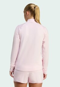 Lyserød langærmet atletisk top med en høj hals og fugttransporterende stof, med glat tekstur og syede detaljer.