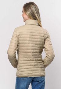 Bēšs pūkains apvalks ar horizontālu šūtu rakstu un augstu apkakli, izgatavots no gluda, viegla materiāla. Valkāts kopā ar zilām džinsu biksēm.