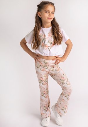 Biały krótki top z kwiatowym wzorem, zestawiony z jasnoróżowymi spodniami w stylu dzwonów z floralnym nadrukiem. Całość uzupełniają białe sneakersy.