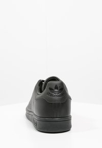 Svarta läder Adidas Stan Smith-sneakers med perforerade sidodekorationer, en texturerad sula och präglad logotyp på hälen.