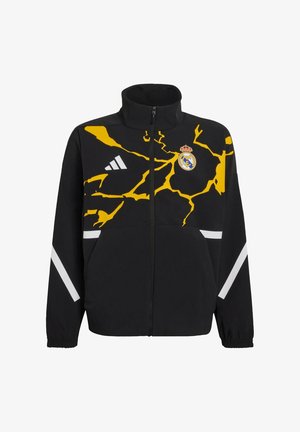 Giacca nera con colletto alto e design a saetta gialla. Presenta un logo del Real Madrid e strisce bianche sulle maniche. Chiusura con cerniera.