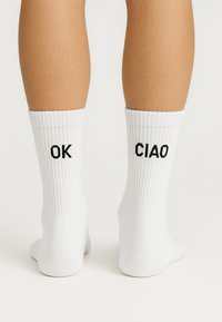 Hvide bomuldsankelsokker med ribbet struktur, der har sort broderede bogstaver "OK" og "CIAO" på siderne.