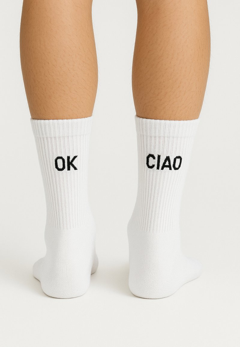 Hvide bomuldsankelsokker med ribbet struktur, der har sort broderede bogstaver "OK" og "CIAO" på siderne.