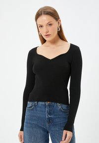 Schwarzes, gestreiftes Langarmtop mit V-Ausschnitt, figurbetontem Schnitt und strukturiertem Stoff, kombiniert mit blauen hochgeschnittenen Jeans.