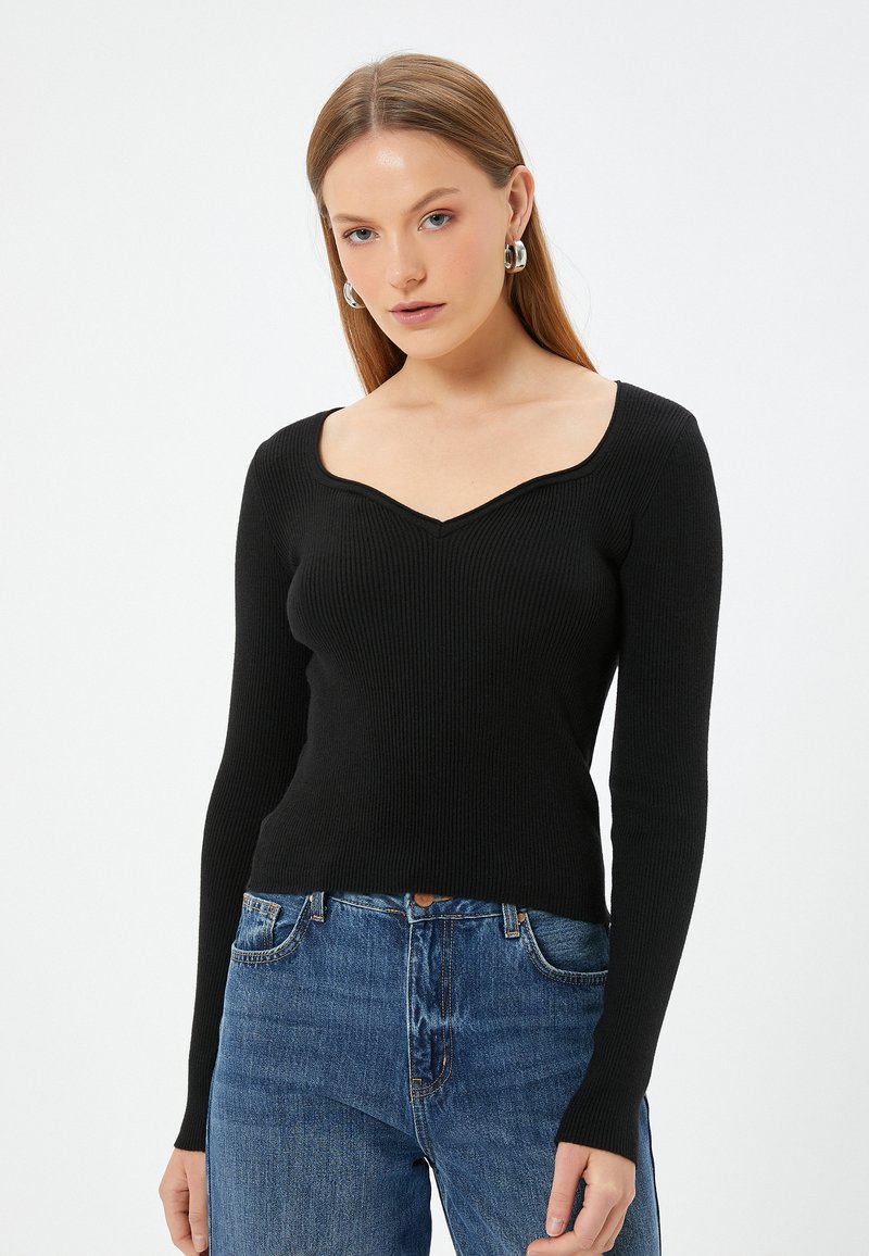 Zwarte geribbelde lange mouw top met een V-vormige halslijn, aansluitend ontwerp en textuurstof, gecombineerd met blauwe high-waisted jeans.
