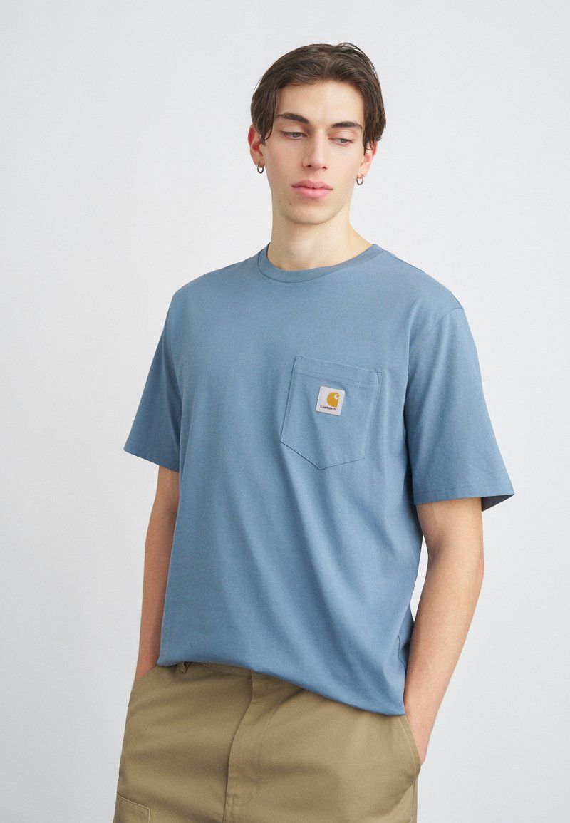 Krátký rukáv, světle modré bavlněné tričko s kulatým výstřihem a kapsou na hrudi; má malou nášivku s logem na kapse.