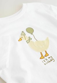 T-shirt en coton blanc avec une illustration d'un canard tenant un ballon vert et portant un chapeau de fête, accompagné du texte "c'est mon anniversaire".