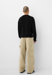 Svart stickad tröja med en kortad design och rå länge, ihopparad med lösa, ljusbeiga cargobyxor med flera fickor.