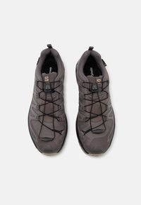Gray hiking shoes with a textured upper, elastic laces, and a cushioned sole. Features a logo and a pull tab at the heel for easy wear.