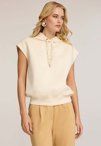 Sudadera de manga corta beige con cuello de cordón, hecha de tejido suave, combinada con pantalones de talle alto amarillos claros.