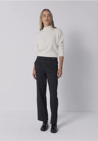 Crème, geribbelde turtleneck trui gecombineerd met zwarte geruite broeken met zijzakken en zilverkleurige hardware, gedragen met zwarte enkellaarsjes.