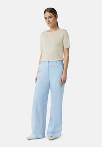 Beige t-shirt met korte mouwen, gecombineerd met lichtblauwe wijde broek. De outfit heeft een relaxte pasvorm, gladde stof en geplooid ontwerp.