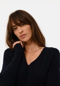 Námořnická modrá, svetr s výstřihem do V a žebrovanými manžetami s měkkou texturou; přiléhavý design s uvolněným střihem kolem výstřihu a ramen.