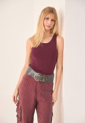 Top sin mangas de canalé burdeos combinado con pantalones holgados de rosa empolvado. El conjunto presenta un cinturón gris con una hebilla grande y tachuelas.